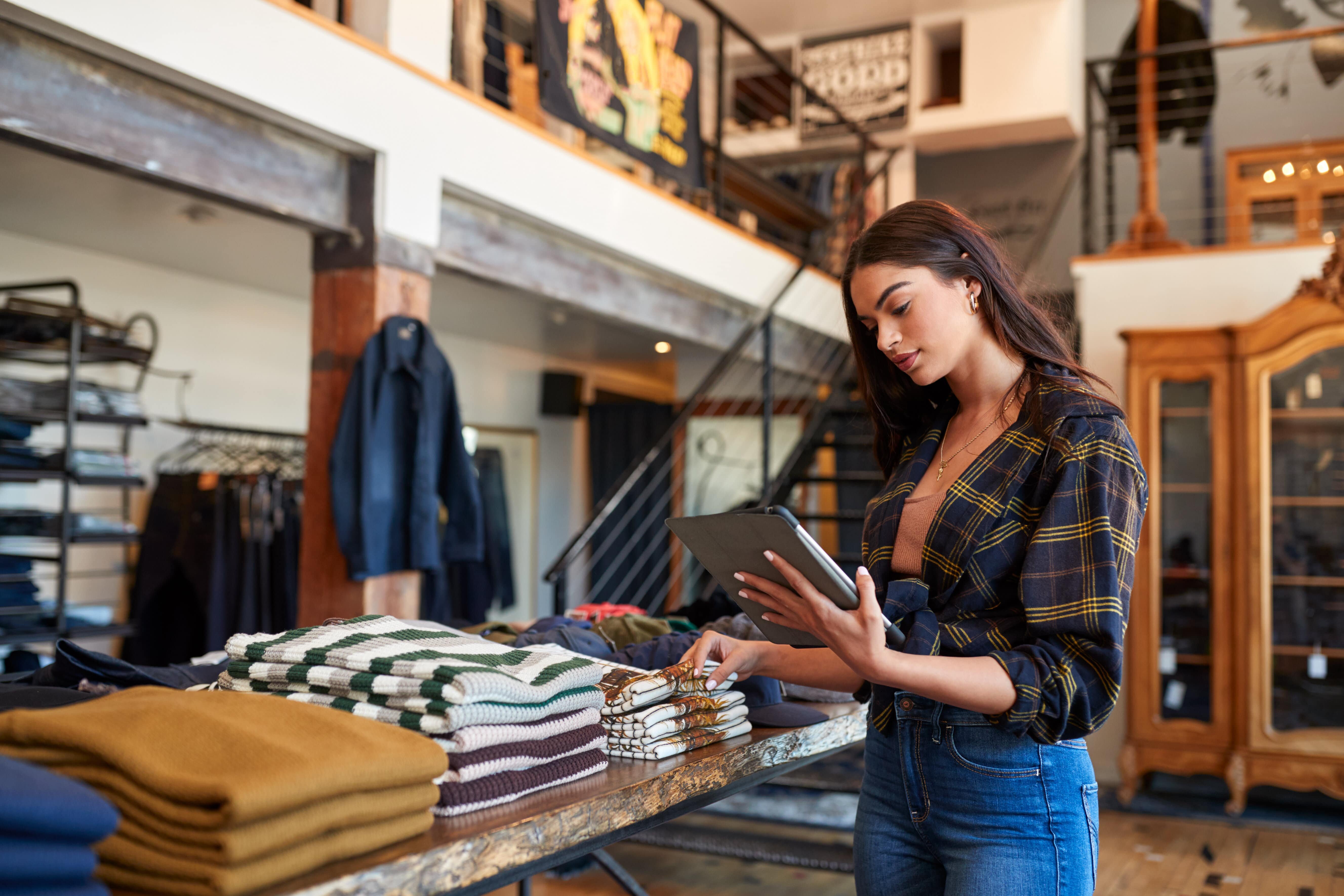 Woman using digital tablet in fashion store reading about retail media